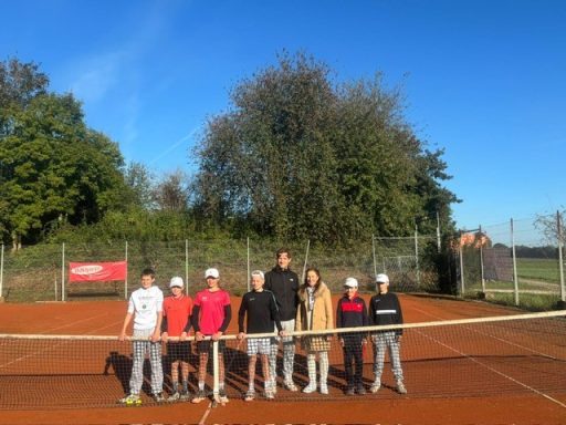 Sechs Kinder und ein Trainer stehen auf einem Tennisplatz unter klarem Himmel.