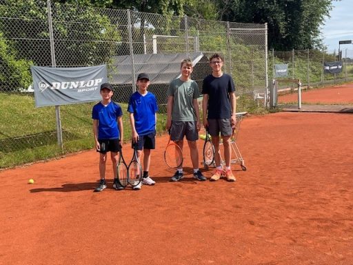 Vier Jungen stehen auf einem Tennisplatz, jeder mit einem Schläger in der Hand.
